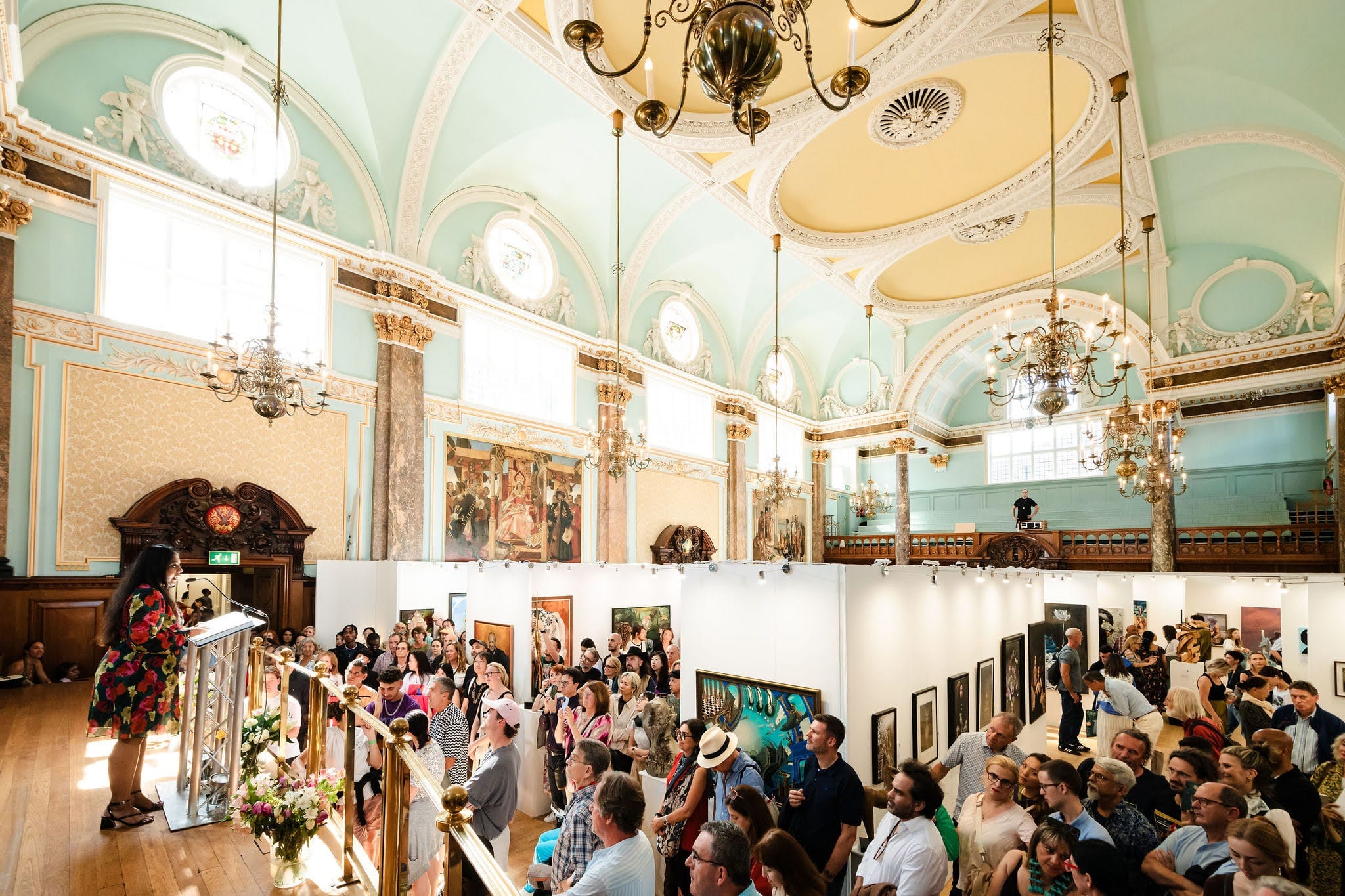 The hall at capacity for an awards ceremony: every aisle taken between the white exhibition walls, the speeches under way.