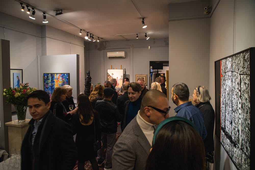 The gallery at capacity, works hung close along both walls.