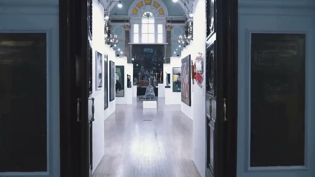 Through the open doors of Chelsea Old Town Hall at the Biennale: a corridor of hung work running away towards the arched window at the end of the hall, a sculpture on a plinth in the middle of the floor.