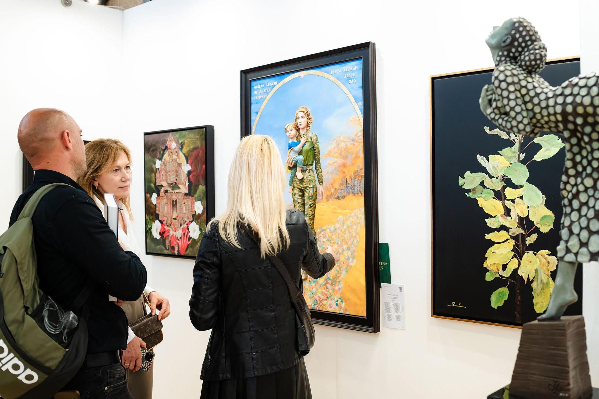 Visitors standing in front of a large framed painting in the exhibition, other works along the wall beside it.