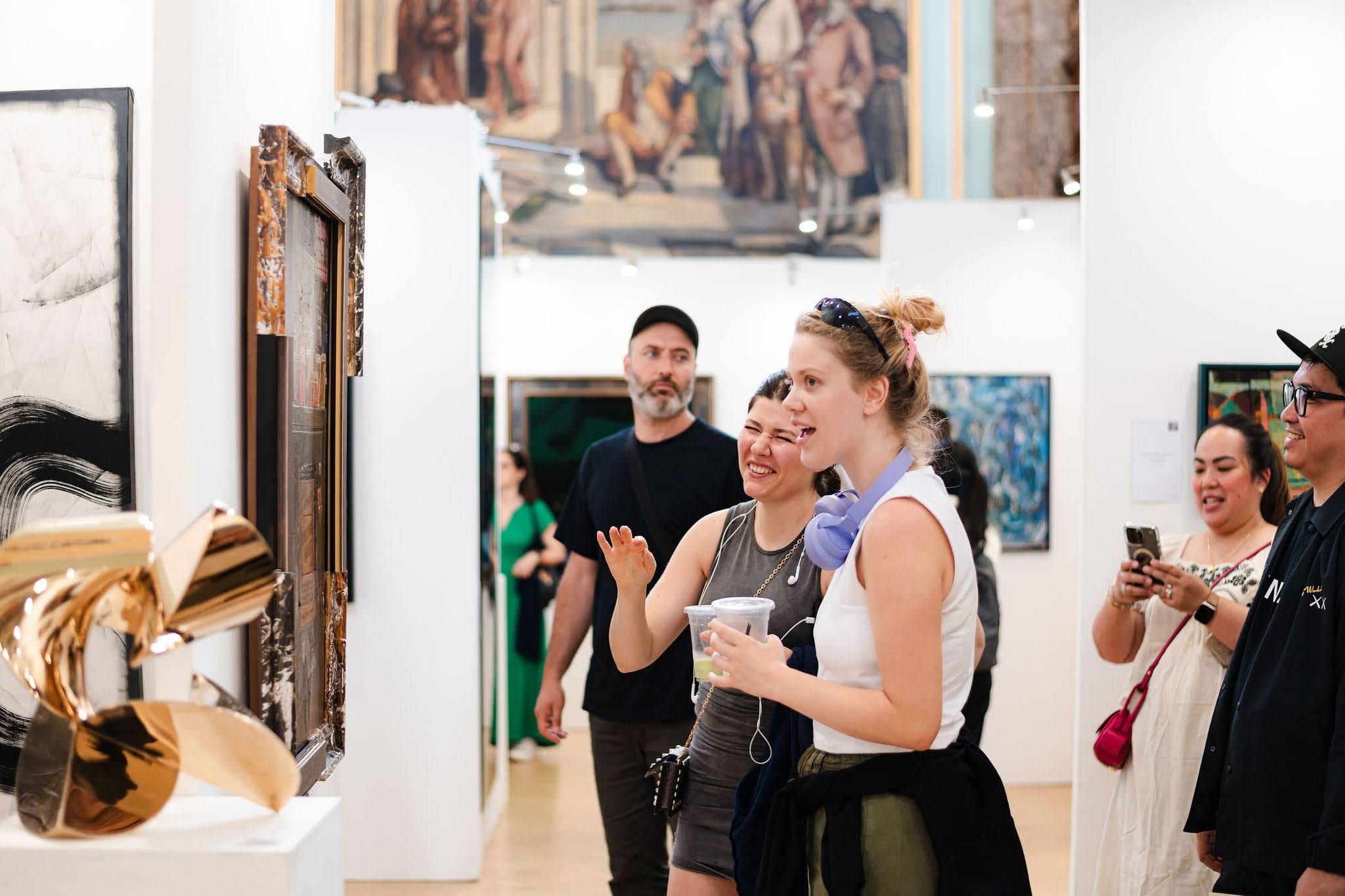 Visitors laughing together in front of a gilded sculpture at the private view, the hang running away behind them.
