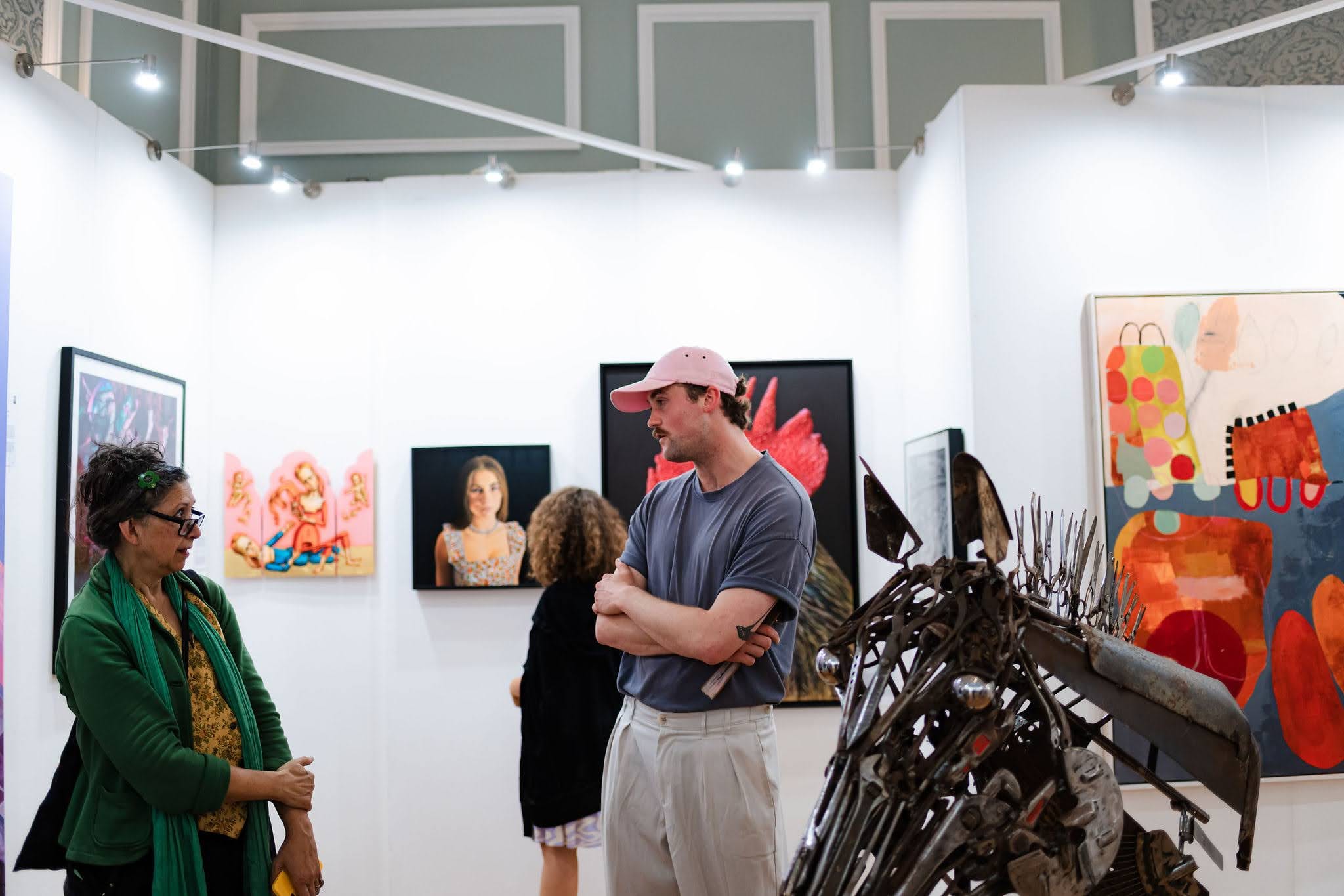 Visitors talking among the hung works, a scrap-metal sculpture in the foreground.